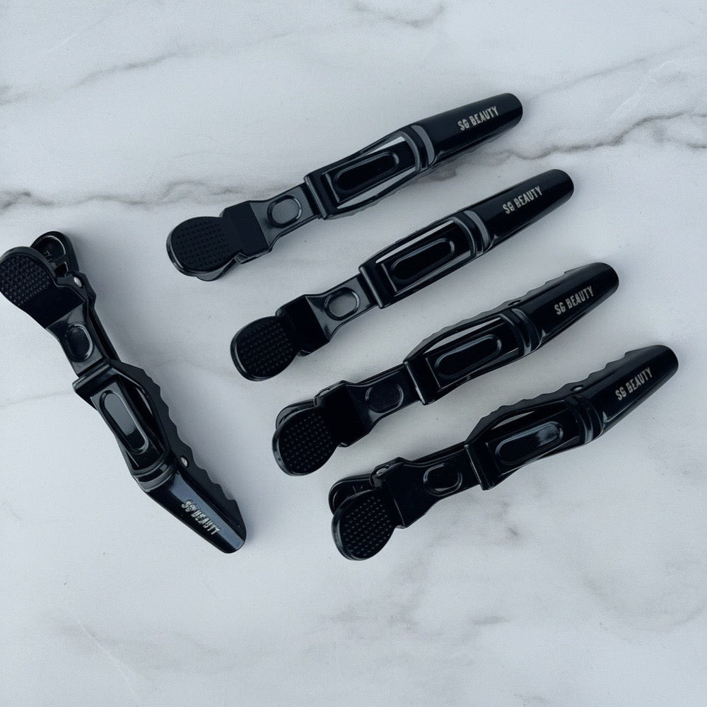 Five black hair claw clips with white '50 BEAUTY' branding, arranged on a white marble background.