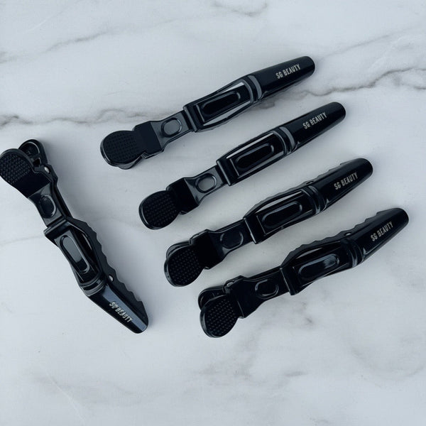 Five black hair claw clips with white '50 BEAUTY' branding, arranged on a white marble background.